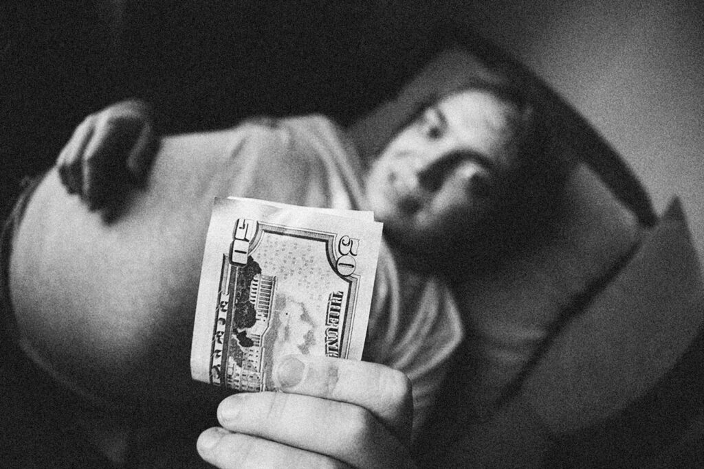 a man laying in bed holding a money bill